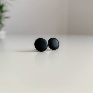 May include: A pair of black round stud earrings. The earrings are simple and minimalist.
