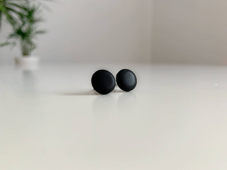 May include: A pair of black round stud earrings. The earrings are simple and minimalist.