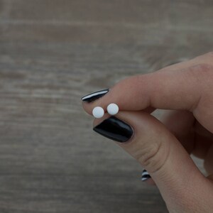 Op de afbeelding: Twee kleine ronde witte pillen die tussen twee vingers met zwarte nagellak worden vastgehouden.