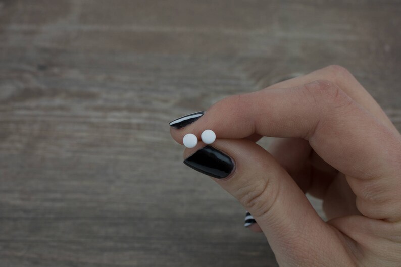 Op de afbeelding: Twee kleine ronde witte pillen die tussen twee vingers met zwarte nagellak worden vastgehouden.