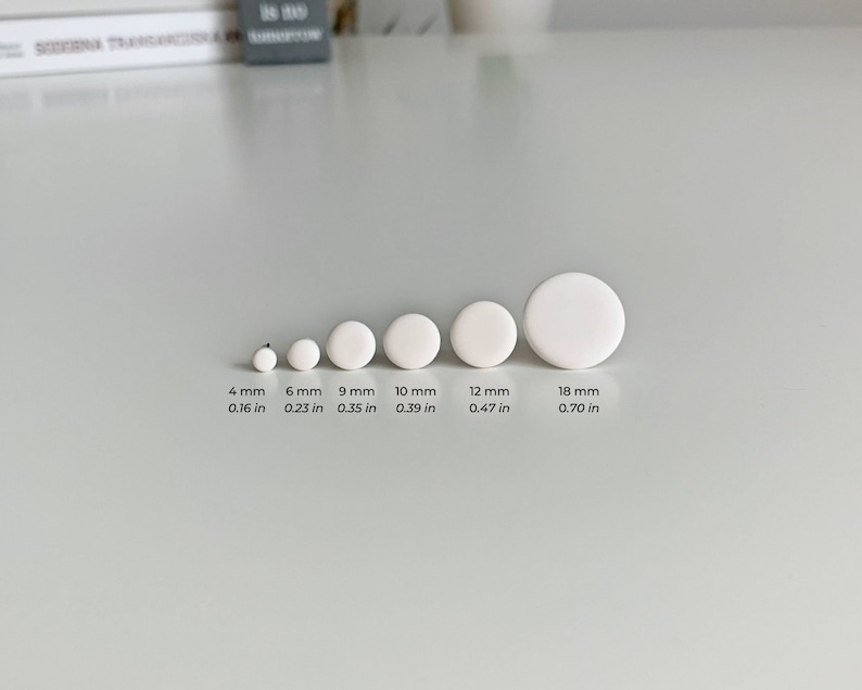 Op de afbeelding: Een set van zes witte ronde keramische schijven in verschillende maten, vari&euml;rend van 4 mm tot 18 mm in diameter. De schijven zijn gerangschikt in een rij van de kleinste tot de grootste, met de afmetingen in millimeters en inches vermeld onder elke schijf.