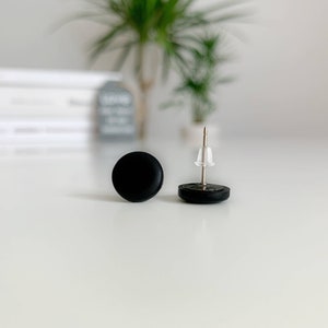 May include: A pair of black stud earrings. The earrings are round and have a simple design.