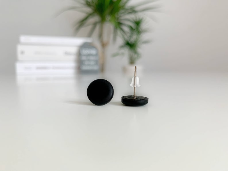 May include: A pair of black stud earrings. The earrings are round and have a simple design.