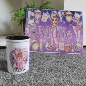 May include: A white ceramic mug with a black rim and a cartoon illustration of a girl with pink hair and a pink dress. The mug has the name "Millie" printed on it. The mug is sitting on a grey surface in front of a glass chopping board with a purple background and a cartoon illustration of a girl with pink hair and a pink dress. The chopping board has the name "Millie" printed on it.