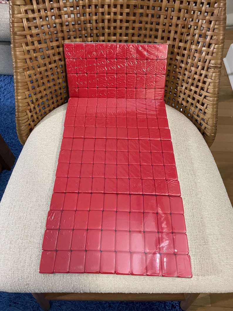 May include: A rectangular set of red mahjong tiles arranged in a grid pattern. The tiles are glossy, solid red, and appear to be wrapped in clear plastic. The set is composed of multiple rows and columns of uniform, smooth, rectangular pieces.
