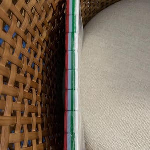 May include: A rectangular object wrapped in clear plastic, featuring a side edge composed of stacked, square-shaped segments. Each segment displays a vertical tricolor pattern of red, white, and green stripes, creating a consistent, repeating design along the entire length of the edge.