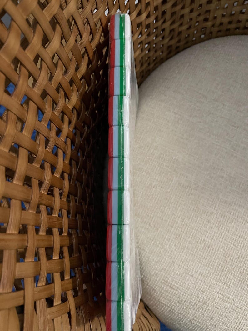 May include: A rectangular object wrapped in clear plastic, featuring a side edge composed of stacked, square-shaped segments. Each segment displays a vertical tricolor pattern of red, white, and green stripes, creating a consistent, repeating design along the entire length of the edge.