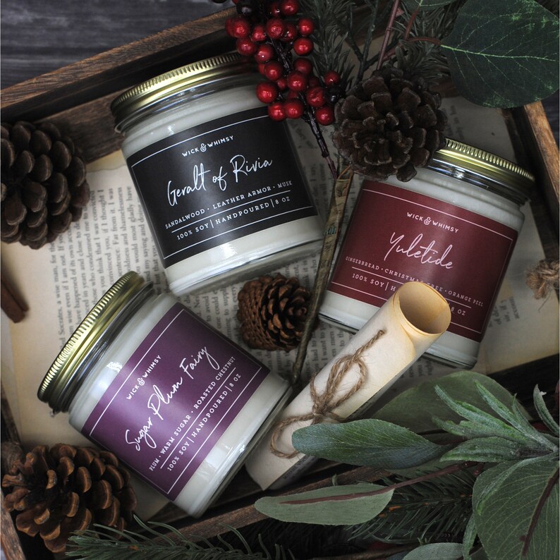 Top down view of 3 candles: Sugar Plum Fairy, Geralt of Rivia, and Yuletide, surrounded by pinecones with book pages as background