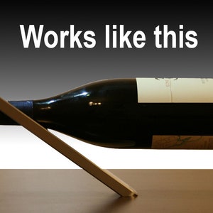 May include: A silver metal wine bottle holder with a bottle of red wine resting on it. The bottle is tilted at an angle and the holder is angled to support the bottle. The text "Works like this" is written in white letters on a black background above the bottle.