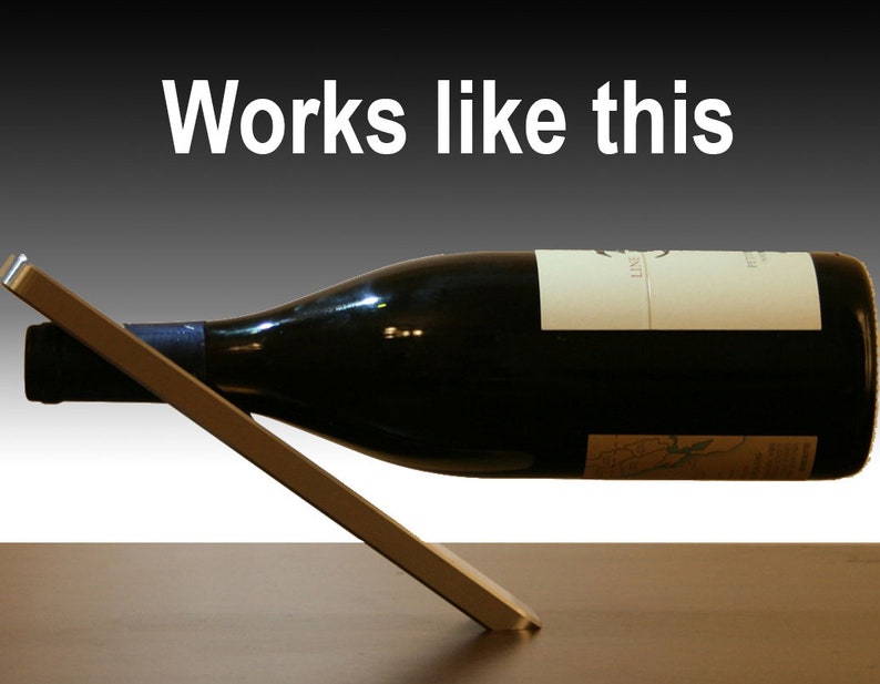May include: A silver metal wine bottle holder with a bottle of red wine resting on it. The bottle is tilted at an angle and the holder is angled to support the bottle. The text "Works like this" is written in white letters on a black background above the bottle.