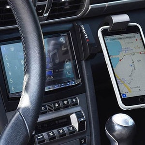 May include: A black car interior with a phone mounted in a Gravity X phone holder. The phone is displaying a map app with a blue route.