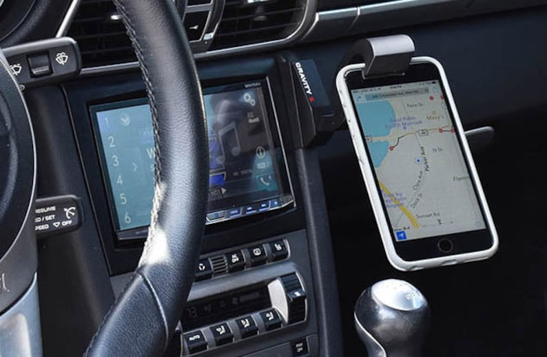May include: A black car interior with a phone mounted in a Gravity X phone holder. The phone is displaying a map app with a blue route.