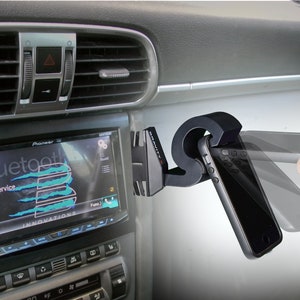 May include: A black car phone mount with a spring-loaded arm to hold a smartphone. The mount is attached to the air vent of the car. The phone is in a black case and the screen is showing the word "Bluetooth" and "No Service".