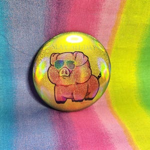 May include: A holographic button with a pink pig wearing sunglasses and the text "SLAY ALL DAY".