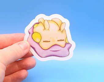 Puede incluir: Una pegatina de dibujos animados amarilla y morada de una babosa de mar durmiendo. La babosa tiene una concha morada y manchas amarillas. La pegatina está sobre un fondo azul.