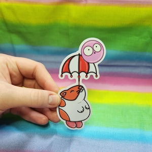 Può includere: Un'illustrazione di un cartone animato di un ombrello a strisce rosse e bianche tenuto da un gatto bianco e arancione con un palloncino rosa con gli occhi attaccato al manico dell'ombrello.