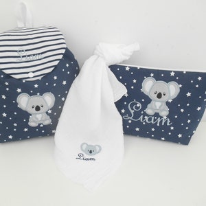 K&ouml;nnte beinhalten: Ein blaues und wei&szlig;es Wickeltaschen-Set mit Koala-Motiv. Das Set beinhaltet einen Rucksack, ein Waschlappen und eine Kosmetiktasche. Alle Artikel sind mit dem Namen "Liam" bestickt.