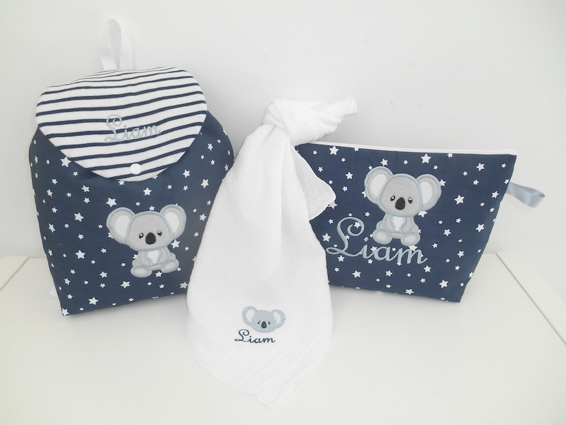 K&ouml;nnte beinhalten: Ein Set aus drei Babyartikeln in einem blau-wei&szlig;en Sternenmuster. Das Set beinhaltet eine Wickeltasche, ein Waschlappen und eine Kosmetiktasche. Jedes Teil ist mit einem grauen Koalab&auml;ren und dem Namen "Liam" bestickt.