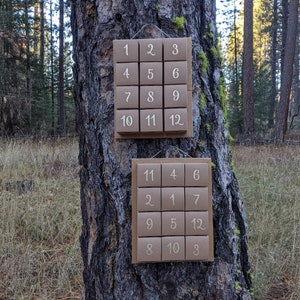 May include: Two rectangular brown cardboard wall hangings, each featuring a grid of twelve small square boxes. The top set displays numbers one through twelve in sequential order, while the bottom set displays the same numbers in a randomized arrangement.