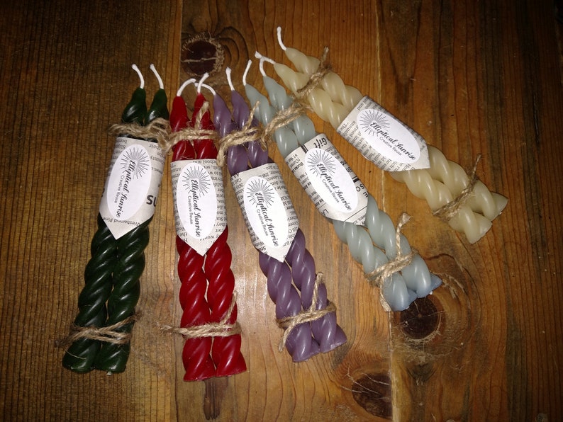 May include: Six twisted candles in various colors, including green, red, purple, and cream, are bundled together with twine. Each candle is labeled with a white sticker that reads "Mystical Sunrise Creative Candles".