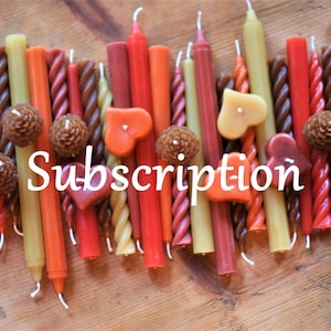 May include: Assortment of colorful, twisted, and straight candles in red, orange, brown, and yellow. The candles are arranged in a row on a wooden surface. The word "Subscription" is written in white text below the candles.