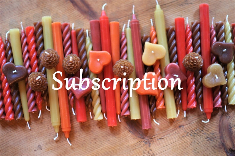 May include: Assortment of colorful, twisted, and straight candles in red, orange, brown, and yellow. The candles are arranged in a row on a wooden surface. The word "Subscription" is written in white text below the candles.