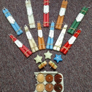 May include: Assortment of taper candles in various colors, including red, blue, green, white, and orange. The candles are bundled together and tied with twine. There are also small star-shaped candles and a box of small round candles.