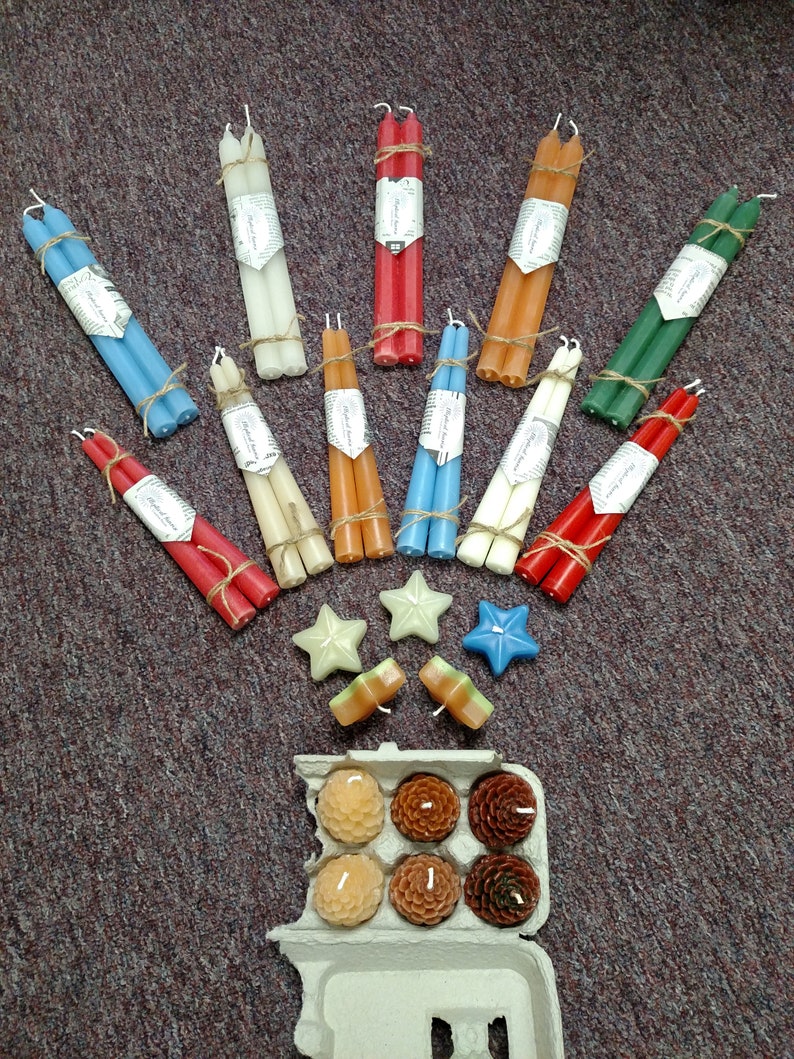 May include: Assortment of taper candles in various colors, including red, blue, green, white, and orange. The candles are bundled together and tied with twine. There are also small star-shaped candles and a box of small round candles.