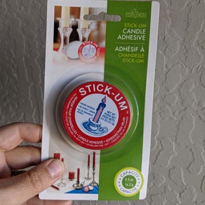 Può includere: Un contenitore bianco con un'etichetta rossa che dice "Stick-Um Candle Adhesive" e un'immagine di una candela. Il contenitore è da 0,5 oz (14,2 g).