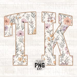 May include: The letters T and K in a block font, filled with a pattern of delicate wildflowers in shades of peach, lavender, and sage green on a white background, outlined in a thin tan border, with a circular logo reading PINK ANCHOR PNG file.