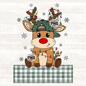 May include: A cartoon reindeer wearing a green plaid hat and a red nose, adorned with Christmas lights. The reindeer is sitting on a green and white plaid rectangle, with snowflakes scattered around it. The image has the text "PINK ANCHOR PNG file".