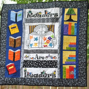 May include: A colorful quilt with a black and white background featuring the text "Readers are Leaders". The quilt has a variety of colorful squares and rectangles with different patterns and designs. The quilt is made of fabric and is likely handmade.