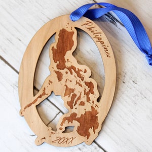 May include: A wooden ornament shaped like the Philippines with the text "Philippines" and "20XX" engraved on it. The ornament is hanging from a blue ribbon.