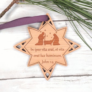 May include: A wooden star-shaped ornament with a laser-engraved image of the nativity scene and the text "In ipso vita erat, et vita erat lux hominum. John 1:4".