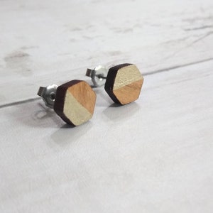 May include: A pair of hexagonal wooden earrings with a two-tone design. One side is a light wood colour, and the other side is a darker wood colour.