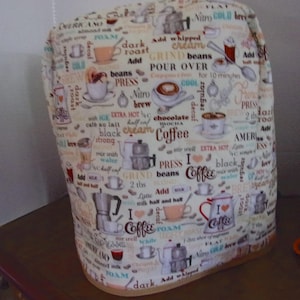 May include: A fabric appliance cover featuring an off-white background with a repeating pattern of coffee-themed illustrations and text including words like Coffee, Espresso, Grind, and Pour Over in various brown, blue, and red fonts.