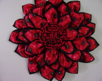 May include: A red fabric flower wreath with black trim. The flower petals are made of fabric with a poppy print.