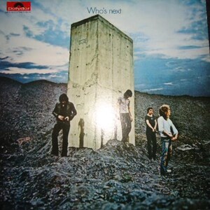 May include: A vinyl record cover titled Who's Next featuring a large concrete monolith standing in a rocky, desolate landscape under a blue sky. Four figures are positioned around the structure, with the Polydor logo visible in the top corner.