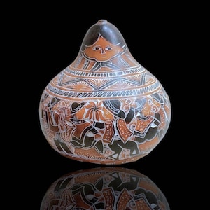 Puede incluir: Una calabaza pintada a mano con un diseño marrón, negro y blanco. La calabaza tiene forma de pera y presenta una cara humana estilizada con un patrón floral alrededor del cuello. La calabaza está decorada con una escena de personas bailando y tocando música.