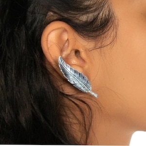 May include: A silver feather ear cuff earring. The earring is designed to sit on the upper part of the ear.