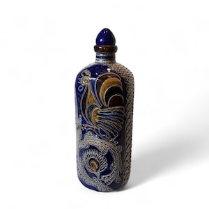May include: A ceramic bottle with a blue, brown, and tan rooster design. The bottle has a dark blue stopper and a textured, patterned side. The rooster is depicted with yellow, brown, and blue feathers, and the bottle has a decorative floral pattern.