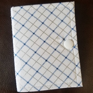 May include: A white fabric pouch with a blue and silver diamond pattern. The pouch has a white snap closure.