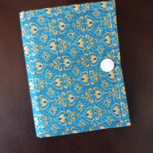 May include: A small blue and gold fabric pouch with a white button closure. The pouch has a repeating pattern of stylized floral designs.
