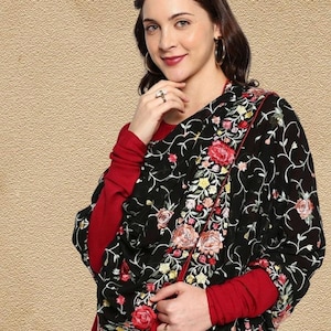 May include: A black shawl featuring intricate floral embroidery in shades of red, pink, yellow, and white, draped over a solid red long-sleeved garment. The shawl has a thin red border and a repeating pattern of vines, leaves, and blooming flowers.