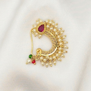 May include: A gold nose ring with a red gemstone and a fringe of white pearls.