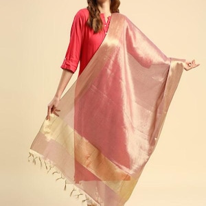 May include: A woman wearing a red tunic and white pants, holding a sheer, pink dupatta. The dupatta has a gold border and tassels. The outfit is a traditional Indian style.