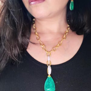 May include: A gold chain necklace featuring a large, pear-shaped green gemstone pendant suspended from two silver-toned, pavé-set links. Matching drop earrings with a silver-toned, pavé-set top and a smaller pear-shaped green gemstone dangle.