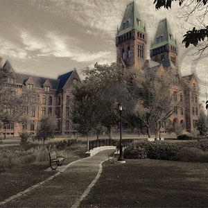May include: A sepia-toned photograph of a large, imposing brick building with two towers. The building has a gothic architectural style and is surrounded by trees and a small bridge. A bench sits on a path leading to the bridge.