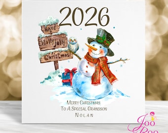 May include: A square greeting card featuring the year 2026, a snowman wearing a black top hat and red plaid scarf, a small owl, and a wooden sign reading Have a Holly Jolly Christmas. Below is text reading Merry Christmas To A Special Grandson Nolan.