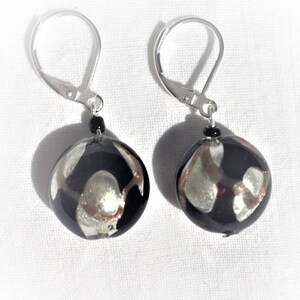 May include: A pair of silver dangle earrings with black and silver round glass beads. The beads have a swirling pattern.
